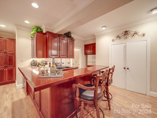 kitchen featuring light hardwood / wood-style floors, crown molding, a kitchen breakfast bar, and kitchen peninsula