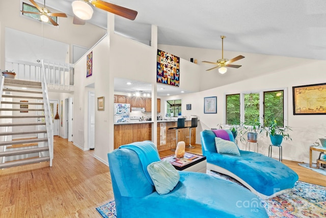 living area featuring light wood-style floors, ceiling fan, high vaulted ceiling, baseboards, and stairs