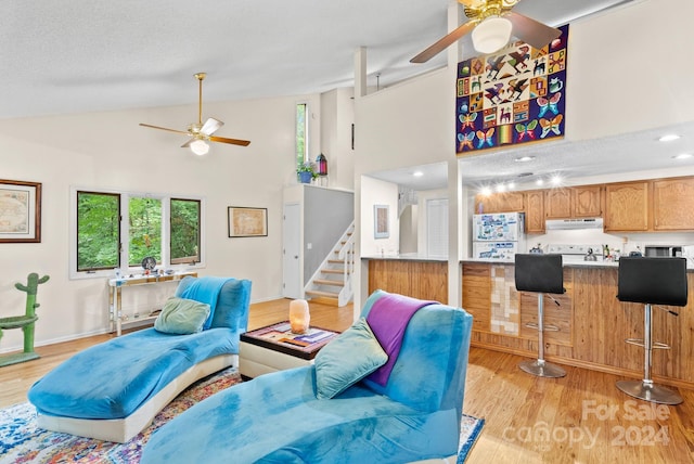 living area featuring a textured ceiling, high vaulted ceiling, ceiling fan, light wood-style flooring, and stairway