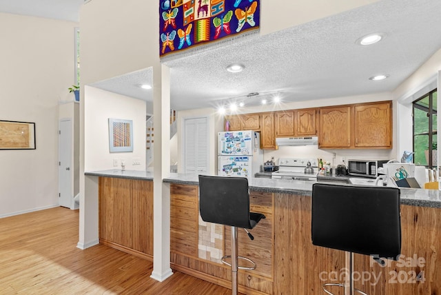 kitchen with a textured ceiling, under cabinet range hood, range with electric cooktop, freestanding refrigerator, and stainless steel microwave