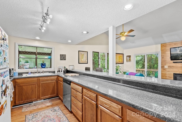 kitchen with light wood-style flooring, brown cabinets, vaulted ceiling, stainless steel dishwasher, and a sink