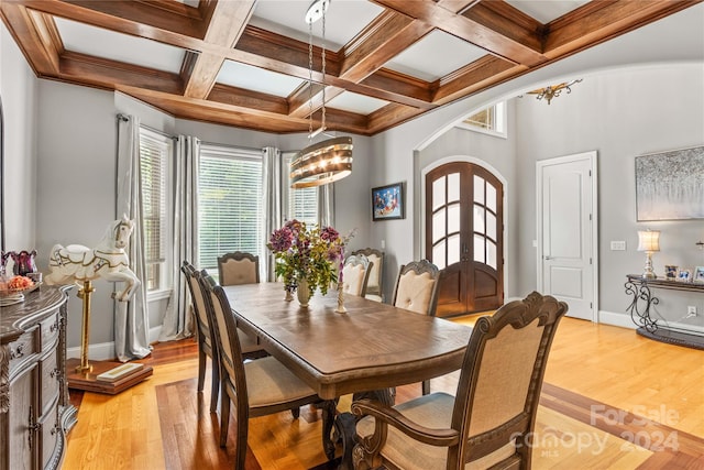 dining space with a notable chandelier, beam ceiling, coffered ceiling, and light wood-type flooring