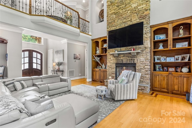 living room with a stone fireplace, light hardwood / wood-style flooring, and a towering ceiling