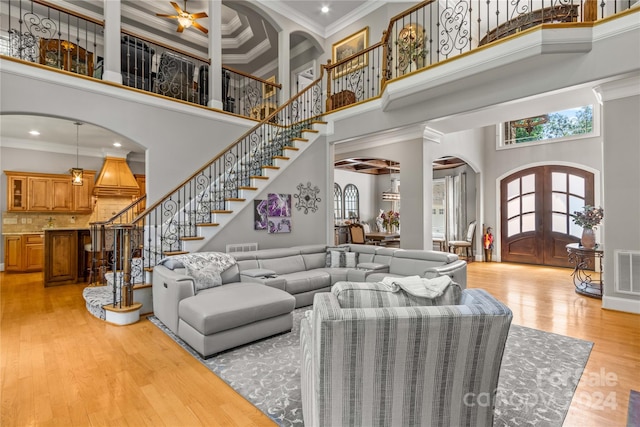 living room featuring ceiling fan, crown molding, french doors, light hardwood / wood-style flooring, and a towering ceiling