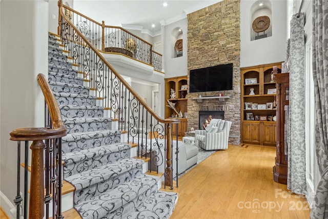 stairway featuring light hardwood / wood-style floors, a fireplace, crown molding, and a towering ceiling