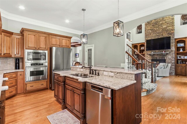 kitchen featuring decorative light fixtures, a fireplace, stainless steel appliances, light wood-type flooring, and sink