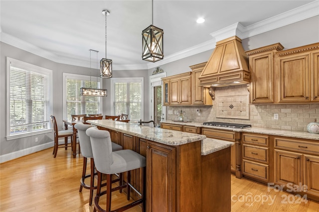 kitchen with a center island with sink, decorative light fixtures, decorative backsplash, light wood-type flooring, and custom range hood