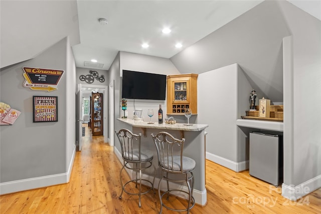 interior space with vaulted ceiling, light hardwood / wood-style flooring, light stone countertops, and fridge