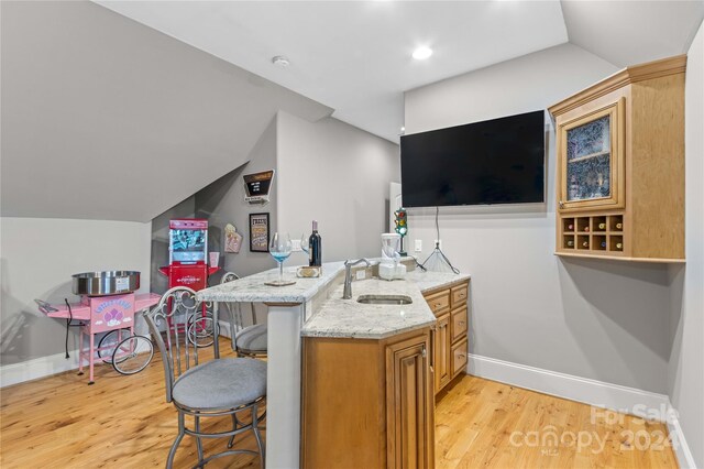 kitchen featuring sink, lofted ceiling, light stone countertops, and light wood-type flooring