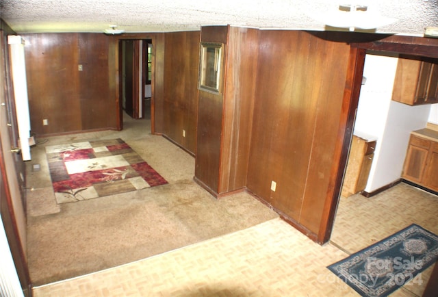 corridor with light colored carpet, a textured ceiling, and wood walls