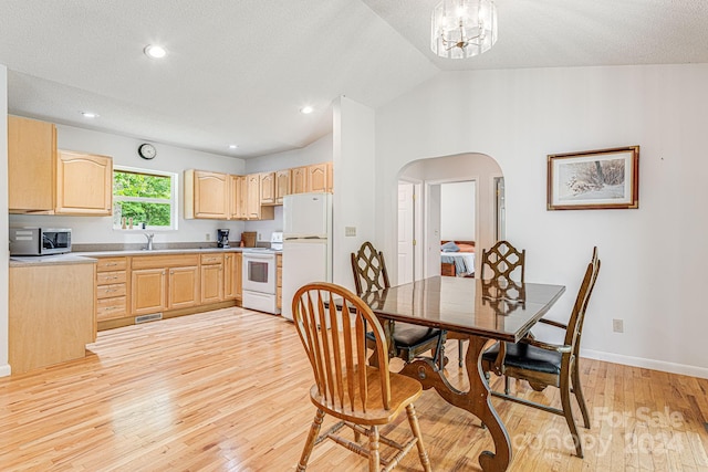 dining room featuring sink, light hardwood / wood-style flooring, a textured ceiling, vaulted ceiling, and a chandelier