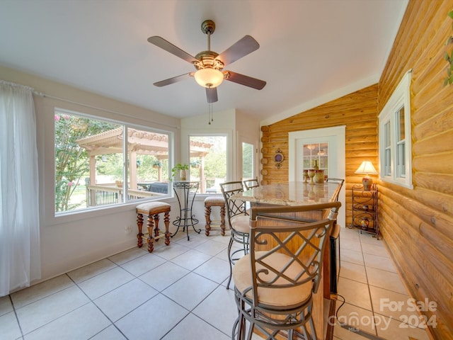 tiled dining space featuring ceiling fan, rustic walls, and vaulted ceiling