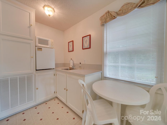 interior space featuring white microwave, refrigerator, white cabinetry, sink, and a textured ceiling