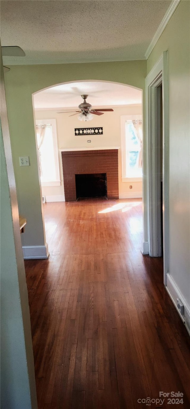 unfurnished living room with a textured ceiling, dark wood-type flooring, ceiling fan, and a brick fireplace