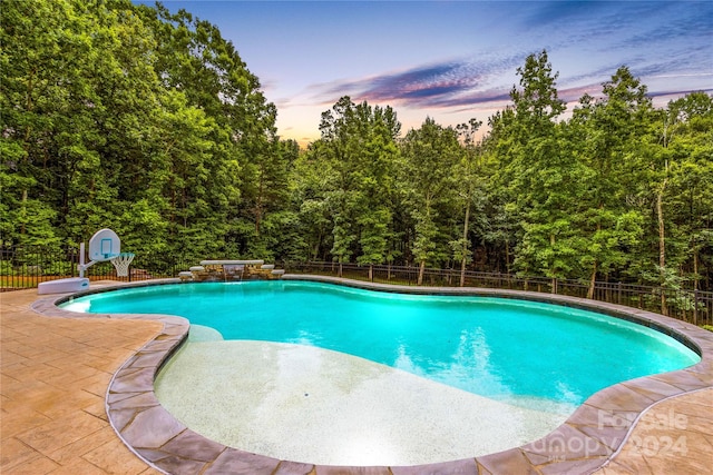 pool at dusk with pool water feature and a patio area