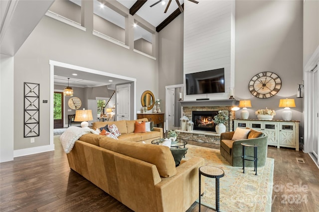 living room featuring a fireplace, wood-type flooring, ceiling fan, a high ceiling, and beam ceiling