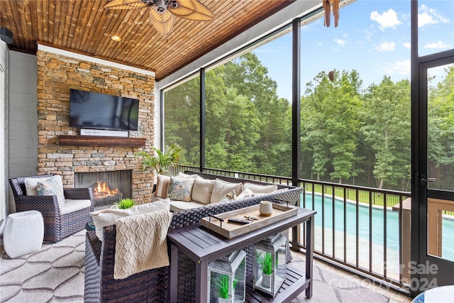 sunroom / solarium with ceiling fan, an outdoor stone fireplace, and wooden ceiling