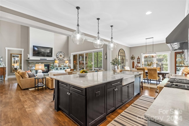 kitchen with wall chimney exhaust hood, dark hardwood / wood-style floors, a wealth of natural light, and an island with sink