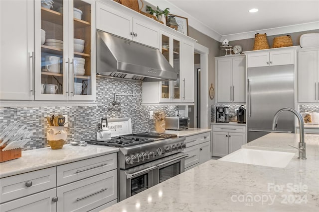 kitchen featuring high quality appliances, light stone countertops, tasteful backsplash, and white cabinetry