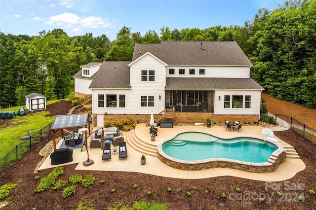 rear view of property featuring a sunroom, a patio, a fenced in pool, and a storage shed