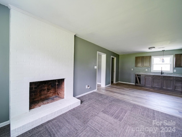 unfurnished living room with light hardwood / wood-style floors, sink, and a brick fireplace