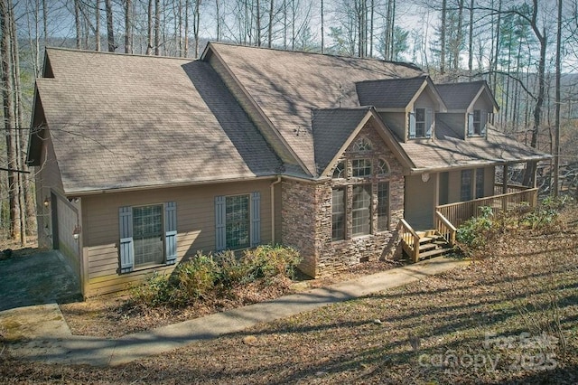 view of front of home featuring stone siding, a shingled roof, and covered porch