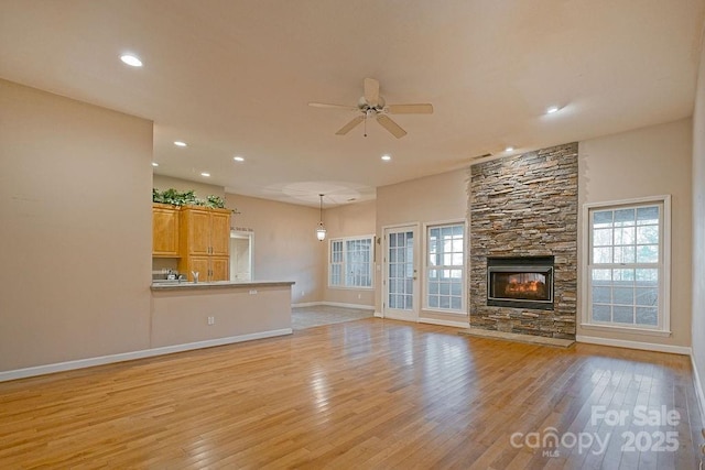 unfurnished living room featuring light wood finished floors, a wealth of natural light, and a stone fireplace