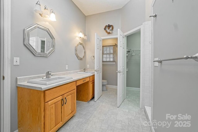 bathroom featuring toilet, double vanity, baseboards, and a sink