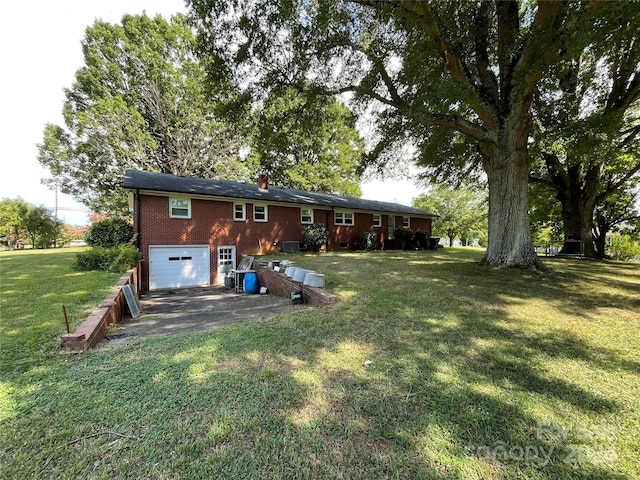 rear view of house with an attached garage, brick siding, a yard, driveway, and a chimney