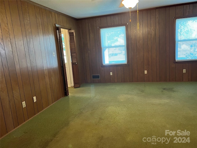 carpeted spare room featuring wooden walls, ceiling fan, and a textured ceiling