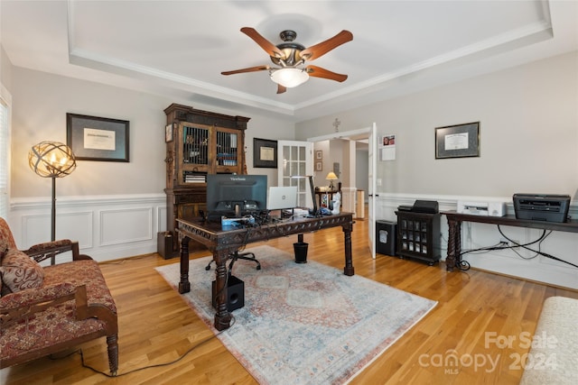 office area with light wood-type flooring, ceiling fan, and a raised ceiling