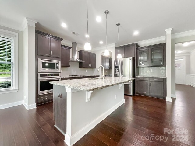 kitchen with crown molding, dark hardwood / wood-style flooring, stainless steel appliances, hanging light fixtures, and wall chimney exhaust hood