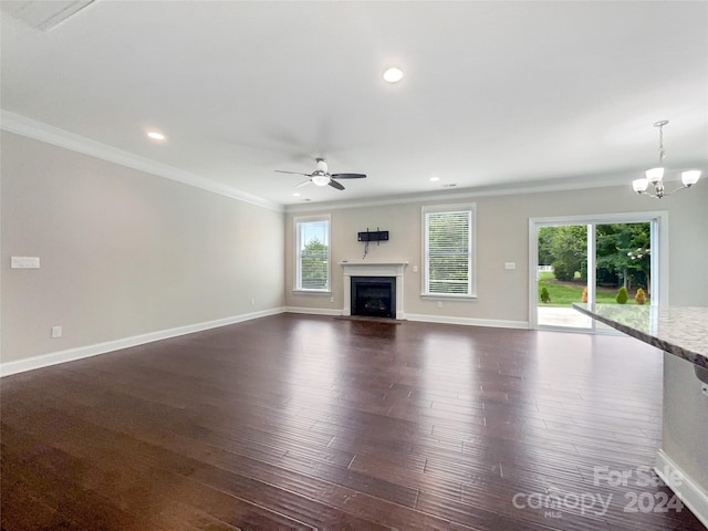 unfurnished living room featuring ornamental molding, ceiling fan with notable chandelier, and dark wood-type flooring