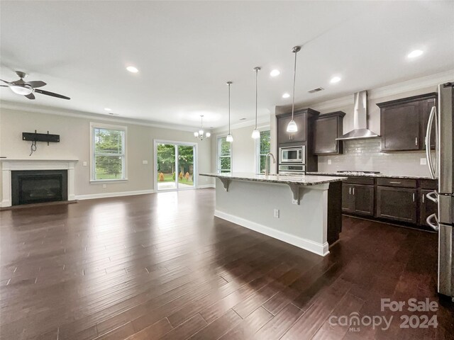 kitchen with tasteful backsplash, dark hardwood / wood-style flooring, appliances with stainless steel finishes, wall chimney exhaust hood, and a kitchen breakfast bar