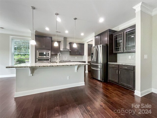 kitchen with tasteful backsplash, wall chimney range hood, stainless steel appliances, dark hardwood / wood-style flooring, and a kitchen breakfast bar