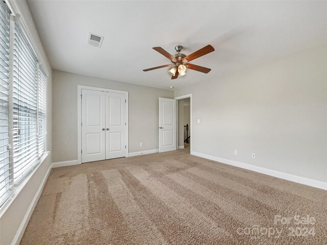 unfurnished bedroom featuring a closet, light colored carpet, and ceiling fan