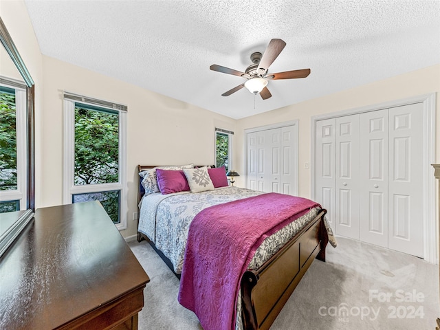 carpeted bedroom with multiple windows, two closets, a textured ceiling, and ceiling fan