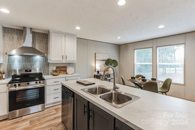 kitchen featuring stainless steel gas stove, light wood-type flooring, wall chimney exhaust hood, sink, and dishwasher