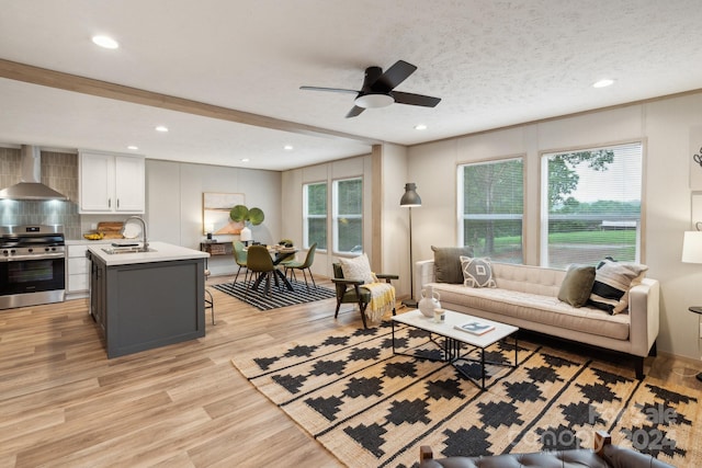 living room with sink, light wood-type flooring, ceiling fan, and a textured ceiling