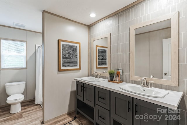 bathroom with ornamental molding, dual vanity, toilet, and tile walls