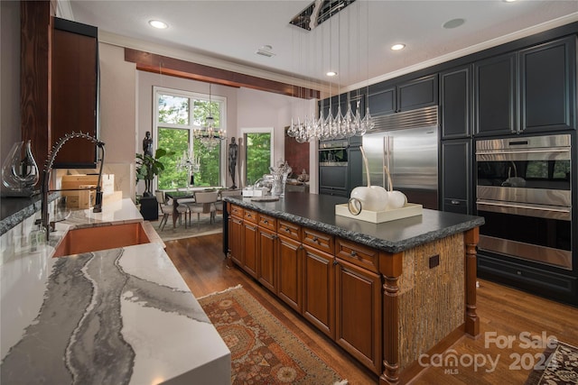 kitchen with sink, stone countertops, hanging light fixtures, appliances with stainless steel finishes, and a kitchen island