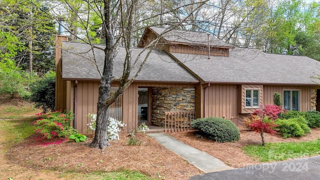 view of front of property featuring stone siding, board and batten siding, a chimney, and roof with shingles