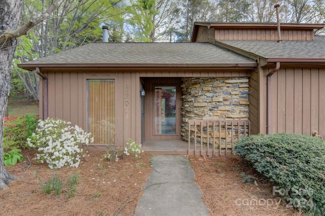 doorway to property featuring stone siding and a shingled roof