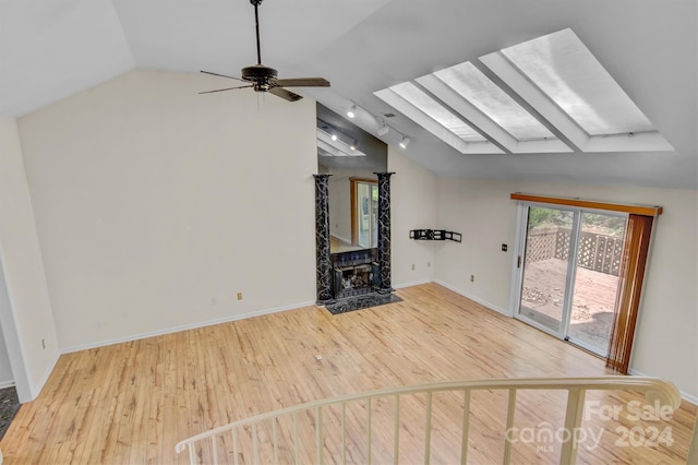 unfurnished living room featuring lofted ceiling with skylight, wood finished floors, baseboards, and ceiling fan