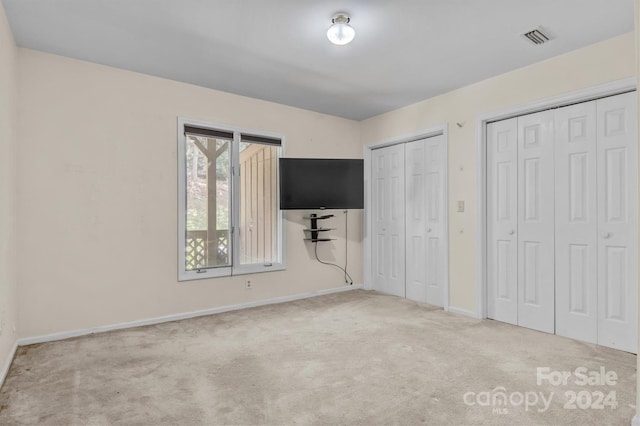 unfurnished bedroom with two closets, visible vents, baseboards, and carpet