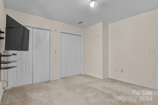 unfurnished bedroom featuring baseboards, carpet floors, two closets, and visible vents