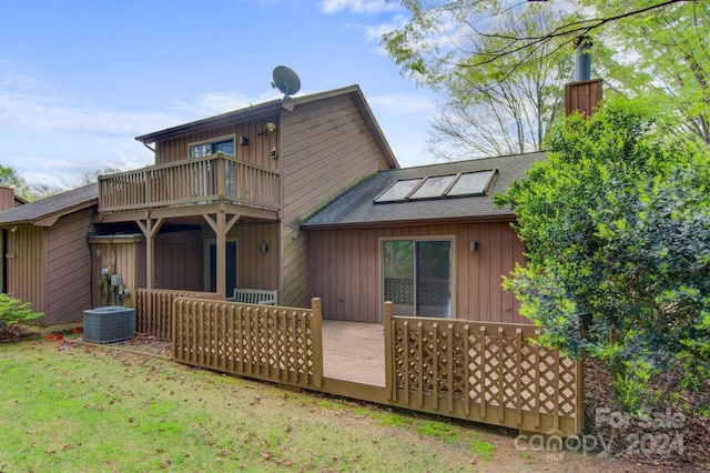 rear view of property with a balcony, cooling unit, roof with shingles, a yard, and a chimney