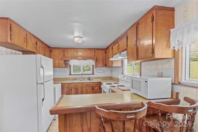 kitchen with a breakfast bar, sink, white appliances, and kitchen peninsula