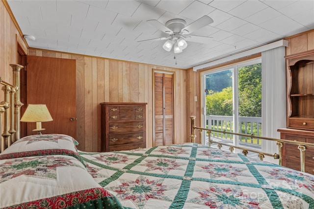 bedroom featuring access to exterior, wooden walls, and ceiling fan