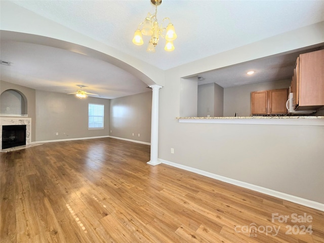 unfurnished living room featuring a fireplace, light hardwood / wood-style floors, ceiling fan with notable chandelier, and ornate columns